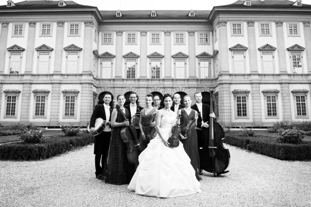 • Das Sisi Salon Ensemble in festlicher Abendkleidung posiert vor einem historischen Gebäude für klassische Live-Musik.